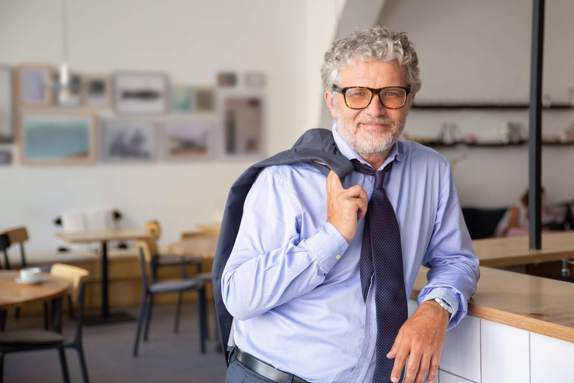 positive-relaxed-mature-business-man-standing-office-cafe-leaning-counter-holding-jacket-shoulder-smiling-camera